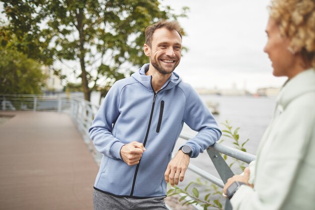 Jonge man in sportkleding praten en glimlachen met jonge vrouw tijdens hun training in het park