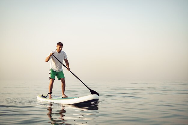 Jonge man in t-shirt en korte broek drijvend op sup board