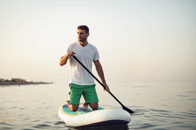 Jonge man in t-shirt en korte broek drijvend op sup board