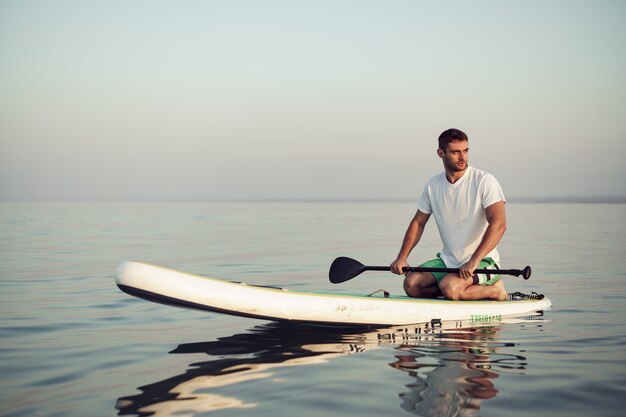 Jonge man in t-shirt en korte broek drijvend op sup board