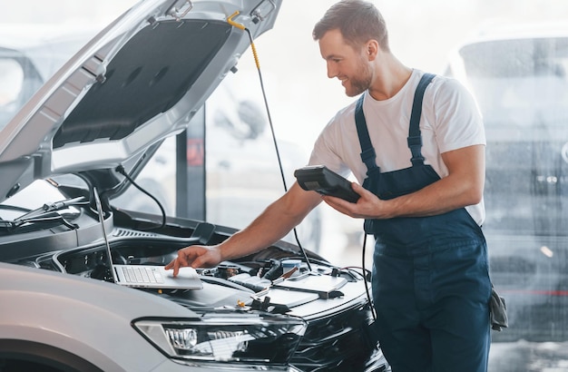 Jonge man in wit overhemd en blauw uniform repareert auto