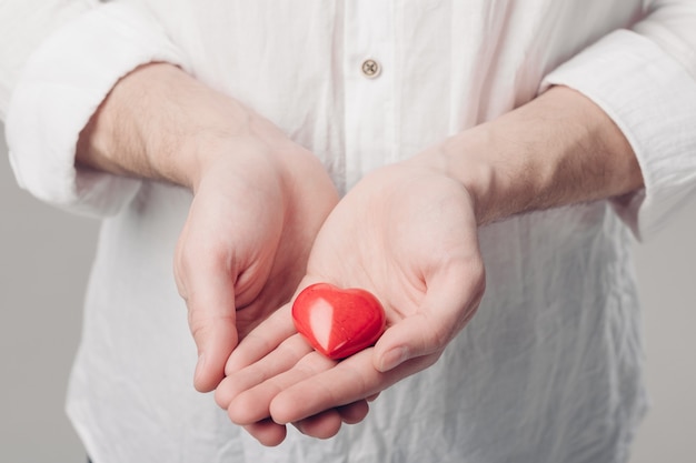 Jonge man in wit overhemd houdt in handen een rood hart op een grijze achtergrond. Valentijnsdag. zacht licht