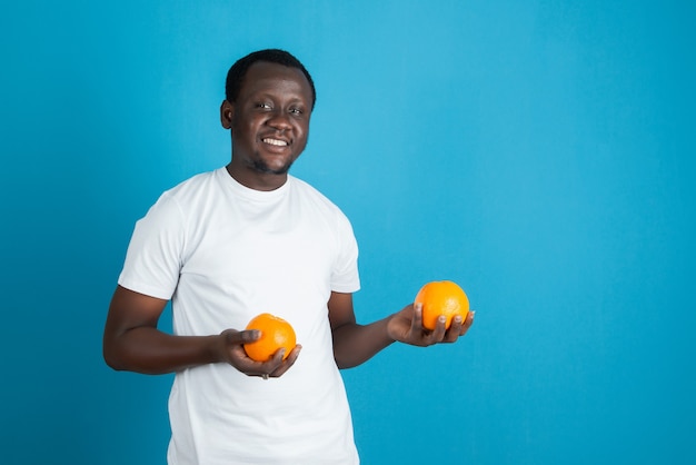 Jonge man in wit t-shirt met twee zoete oranje vruchten tegen blauwe muur