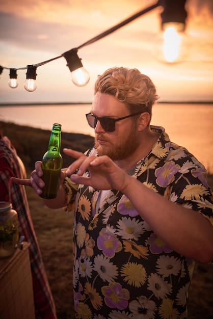 Jonge man in zonnebril bier drinken en dansen tijdens een feestje op het strand