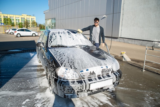 Jonge man in zonnebril wassen auto bij selfservice carwash