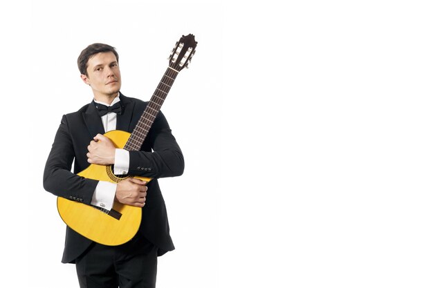 jonge man in zwart klassiek pak met vlinderdas poseren met klassieke gitaar in studio op wit