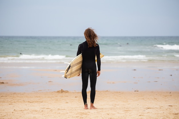 Jonge man in zwarte wetsuit op het strand met surfplank overdag