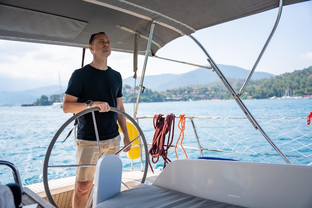 Jonge man kapitein staat aan het roer en bestuurt een zeilboot tijdens een reis over zee