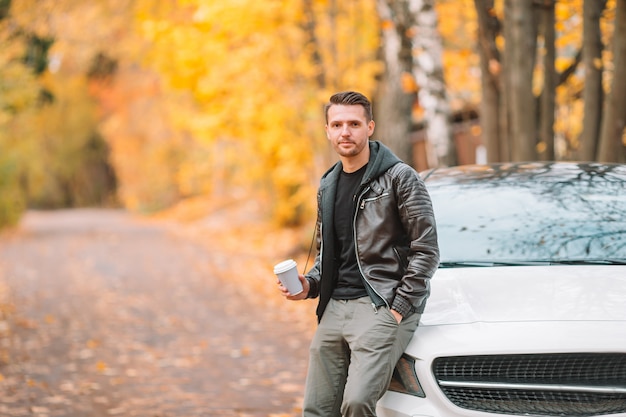 Jonge man koffie drinken met telefoon in herfst park buitenshuis