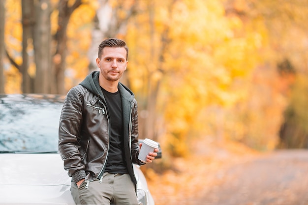 Jonge man koffie drinken met telefoon in herfst park buitenshuis