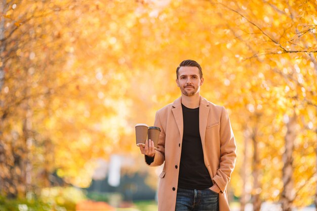 Jonge man koffie drinken met telefoon in herfst park buitenshuis