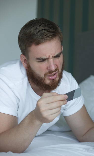 Foto jonge man lag in bed en keek naar het concept van de creditcard om geld te besparen op internet