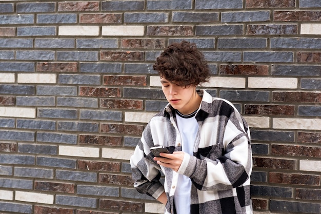 Jonge man leest bericht op telefoon tegen een bakstenen muur