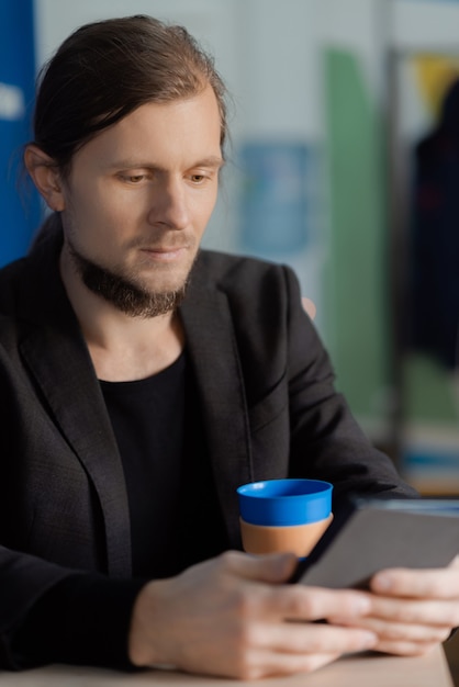 Jonge man leest een nieuw boek op zijn tablet met een kopje koffie