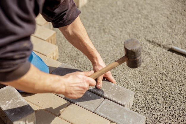 Jonge man legt grijze betonnen bestrating platen in huis binnenplaats op grind funderingsbasis Meester legt straatstenen Tuin baksteen pad bestrating door professionele bestratingswerker trottoir repareren