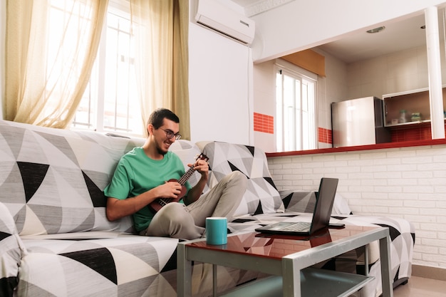 Foto jonge man leren om de ukelele online te spelen vanaf zijn bank