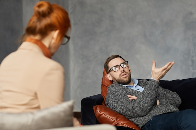 Jonge man liggend op de bank en tijdens zijn bezoek aan de psycholoog te praten over zijn probleem