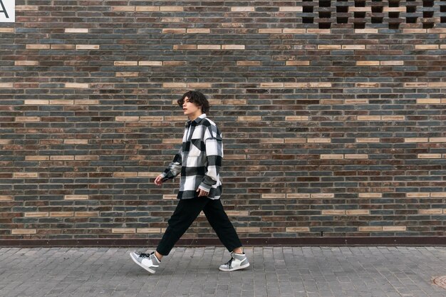 Jonge man loopt de straat af voor een bakstenen muur.