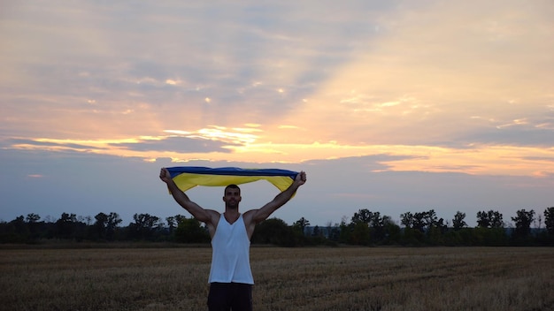 Jonge man loopt met een nationale blauwe gele banier op een gerstweide bij zonsopgang