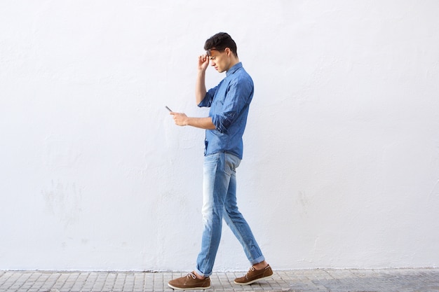 Jonge man lopen en lezen SMS-bericht op mobiele telefoon