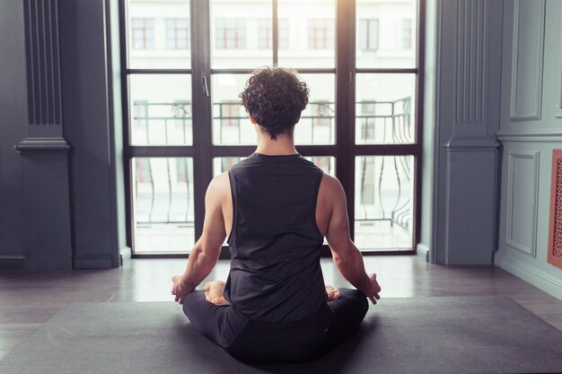 Jonge man mediteert tijdens het beoefenen van yoga in lotushouding achteraanzicht