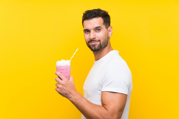 Jonge man met aardbeimilkshake over geïsoleerde gele muur