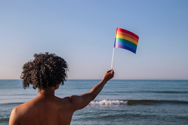 Foto jonge man met afrohaar heft een wimpel op met lgtbi-kleuren