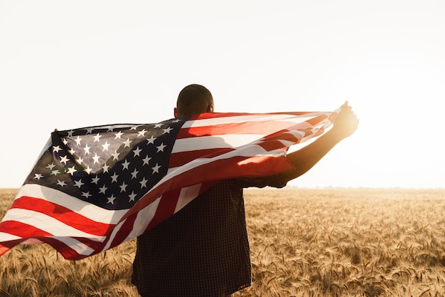 Jonge man met Amerikaanse vlag op zijn rug terwijl hij in een tarweveld staat