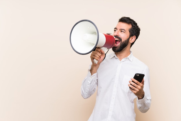 Jonge man met baard met een mobiel schreeuwen door een megafoon