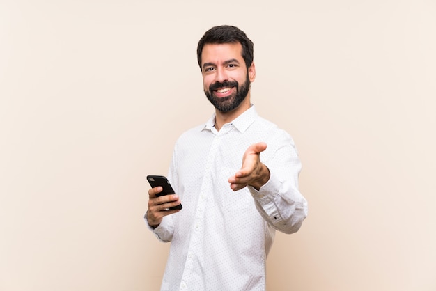 Jonge man met baard met een mobiele handen schudden voor het sluiten van een goede deal