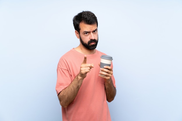 Jonge man met baard met een take-away koffie over geïsoleerde blauw gefrustreerd en wijzend naar de voorkant