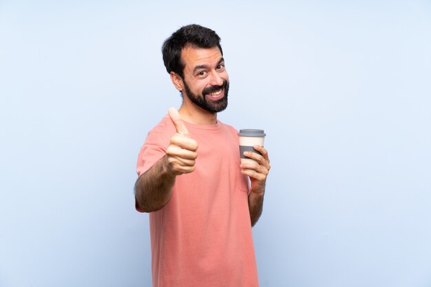 Jonge man met baard met een take-away koffie over geïsoleerde blauw met duimen omhoog omdat er iets goeds is gebeurd