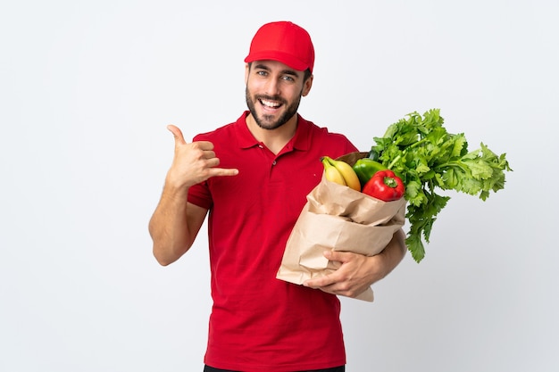 Jonge man met baard met een zak vol groenten geïsoleerd op een witte achtergrond telefoon gebaar maken