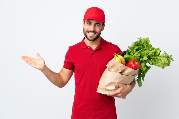 Jonge man met baard met een zak vol groenten geïsoleerd op wit kopie ruimte denkbeeldig op de palm te houden