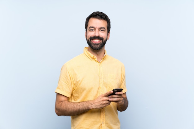 Jonge man met baard op blauw die een bericht verzendt met mobiel