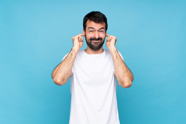 Jonge man met baard over geïsoleerde blauw gefrustreerd en die oren bedekt