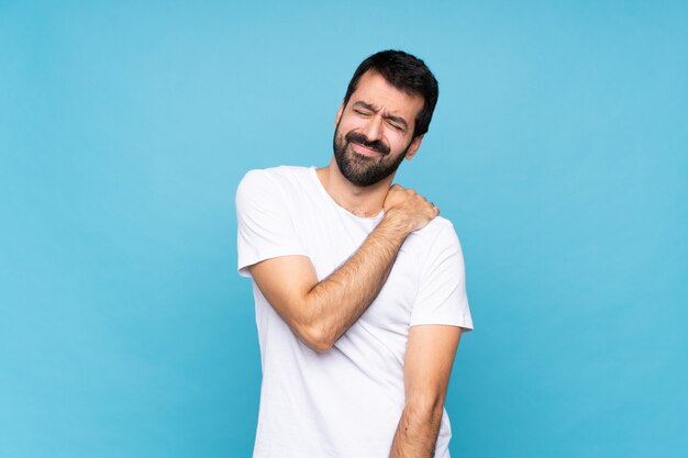 Jonge man met baard over geïsoleerde blauw lijden aan pijn in de schouder voor het hebben gedaan van een inspanning