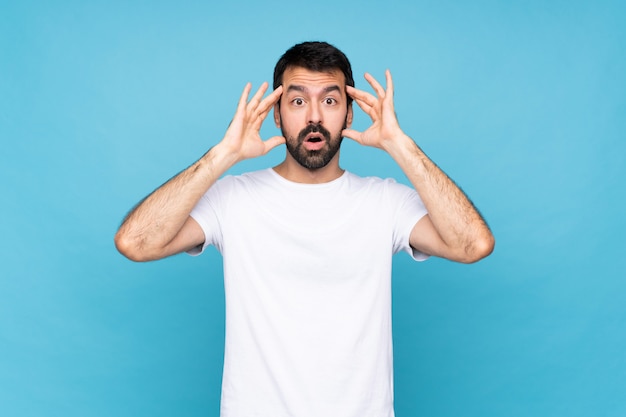 Jonge man met baard over geïsoleerde blauw met verrassing expressie