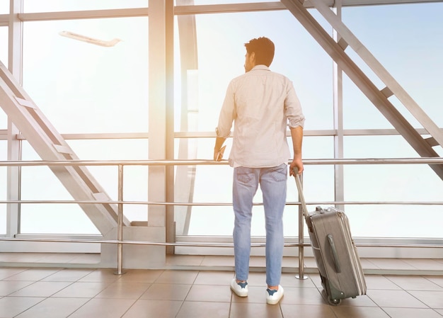 Jonge man met bagage genietend van uitzicht op het raam op de luchthaven