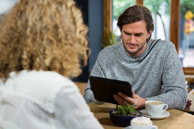 Jonge man met behulp van digitale tablet met vrouw op voorgrond bij koffiehuis