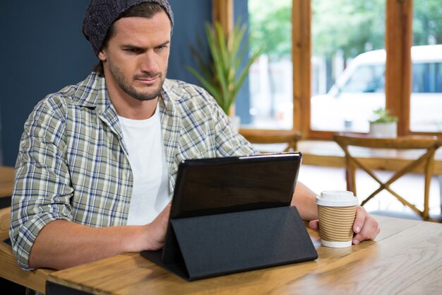 Jonge man met behulp van digitale tafel tijdens het drinken van koffie in café