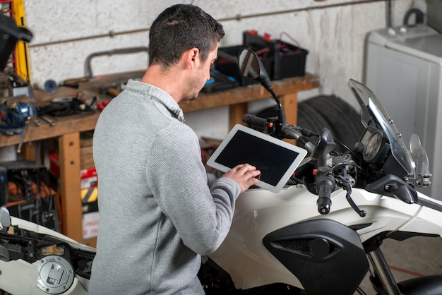 Jonge man met behulp van een tablet naast motorfiets