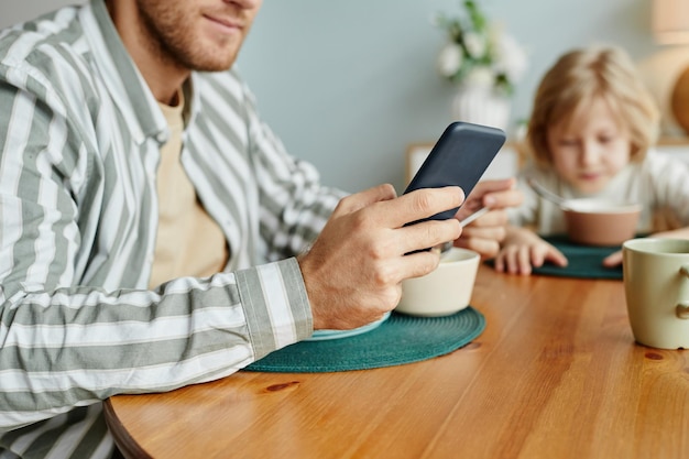 Jonge man met behulp van smartphone bij het ontbijt close-up