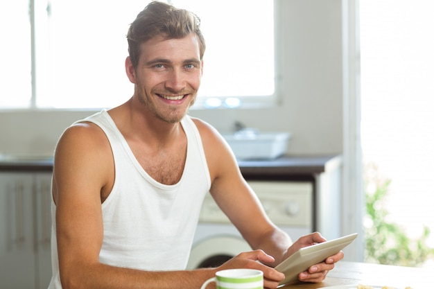 Jonge man met behulp van tablet-pc aan de ontbijttafel