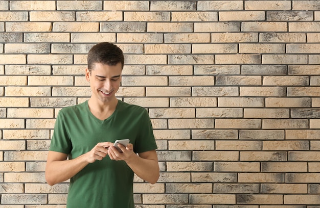 Jonge man met behulp van telefoon op bakstenen muur achtergrond