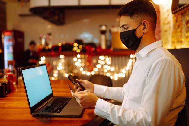 Jonge man met beschermend gezichtsmasker die tijdens de wintervakantie op laptop thuis werkt