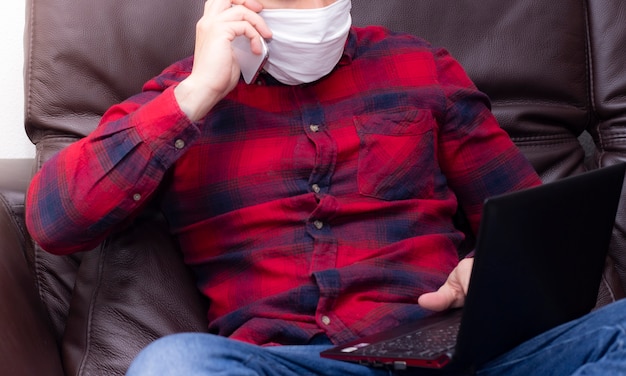 Jonge man met beschermend masker interactie met zijn smartphone binnenshuis voor quarantaine. zelfisolatie voor covid-19
