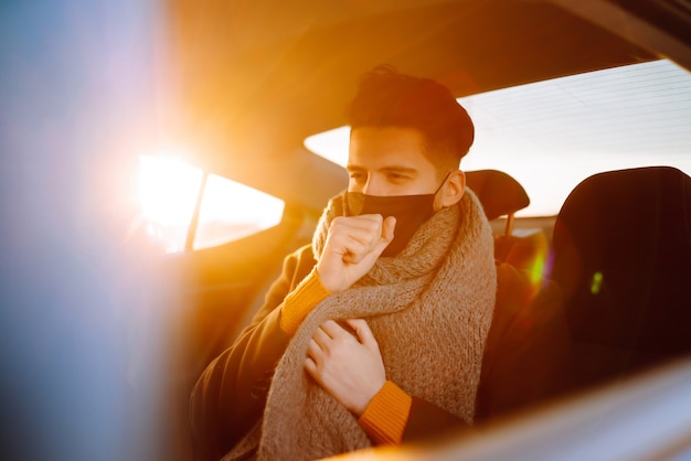 Jonge man met beschermend steriel masker in taxi-auto op een achterbank die haar mobiele telefoon controleert.