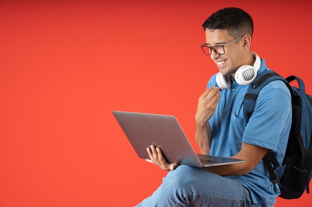 Jonge man met bril en koptelefoon die met gekruiste benen zit, blij en lachend terwijl hij een videogesprek voert op een laptop