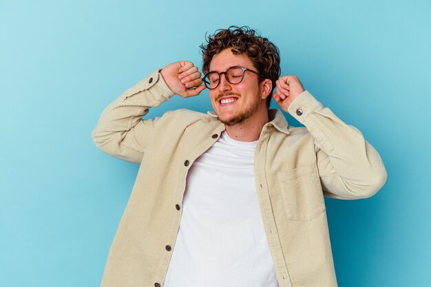 Jonge man met bril geïsoleerd op blauwe muur viert een speciale dag, springt en heft de armen op met energie